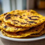 A stack of four golden yellow, slightly charred soft corn tortillas resting on a white plate.