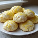 A pile of soft ricotta cookies drizzled with white glaze and topped with bright yellow lemon zest.
