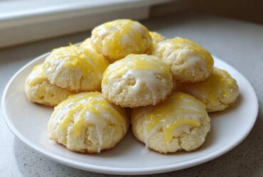 A pile of soft ricotta cookies drizzled with white glaze and topped with bright yellow lemon zest.