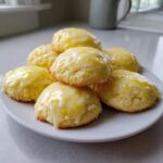 A stack of soft, round ricotta cookies topped with a thick, dripping lemon glaze and zest.