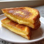 Two halves of golden brown sourdough french toast stacked, oozing with creamy filling.