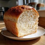 A loaf of freshly baked sourdough sandwich bread, cut to show the soft, fluffy interior and golden crust.