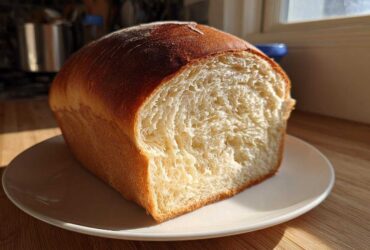 A freshly baked loaf of sourdough sandwich bread, sliced to show the soft, fluffy interior crumb.