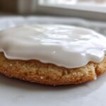 Close-up of a golden sugar cookie topped with thick, glossy white cookie icing.