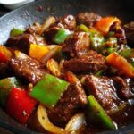 Close-up of tender pepper steak mixed with colorful bell peppers and onions coated in a rich brown sauce.