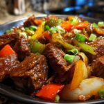 Close-up of tender pepper steak cubes coated in a rich sauce with colorful bell peppers and onions.