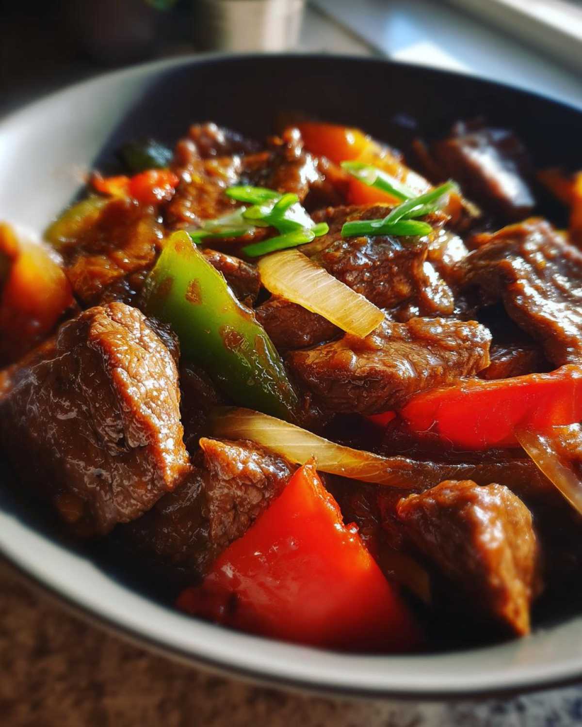 Close-up shot of tender pepper steak pieces coated in a rich sauce with red and green bell peppers and onions.