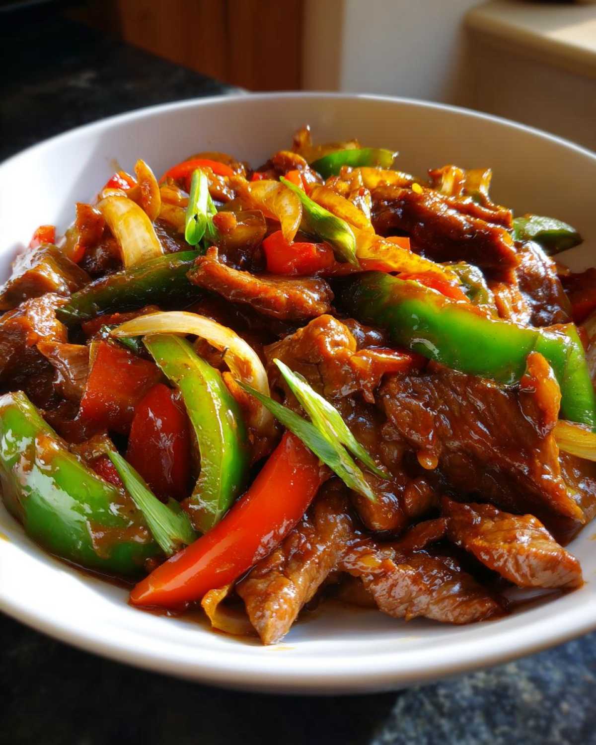 Close-up of glossy, saucy pepper steak strips mixed with vibrant green and red bell peppers and onions.