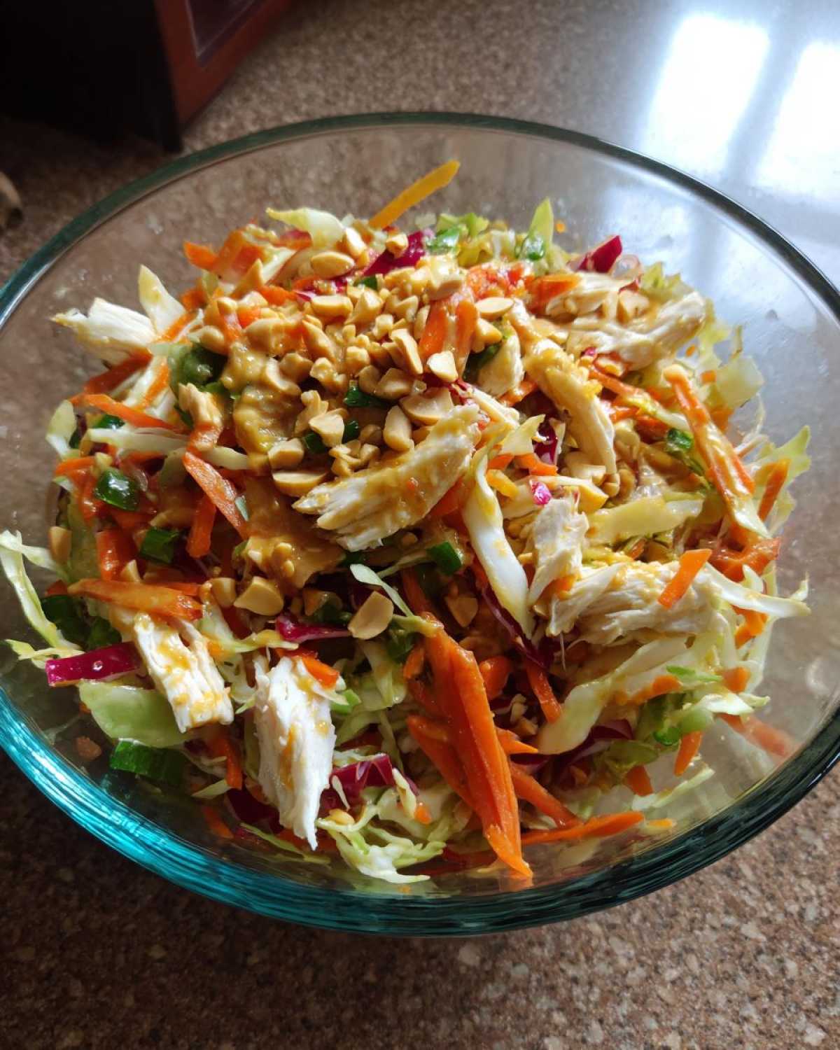 A close-up view of a vibrant thai chicken salad featuring shredded chicken, cabbage, carrots, and peanut dressing topped with chopped peanuts.