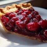 A close-up of a slice of pie generously topped with thick cherry pie filling and whole cherries.