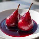 Close-up of two beautifully vibrant red poached pears sitting in a pool of dark red poaching liquid.