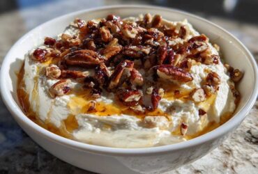 A white bowl filled with creamy whipped goat cheese topped with candied pecans and drizzled with honey.