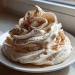 A beautiful swirl of whipped honey butter recipe, dusted lightly with cinnamon, served on a small white plate.