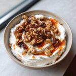 A close-up of a bowl of creamy whipped ricotta dip topped generously with glazed walnuts and drizzled honey.