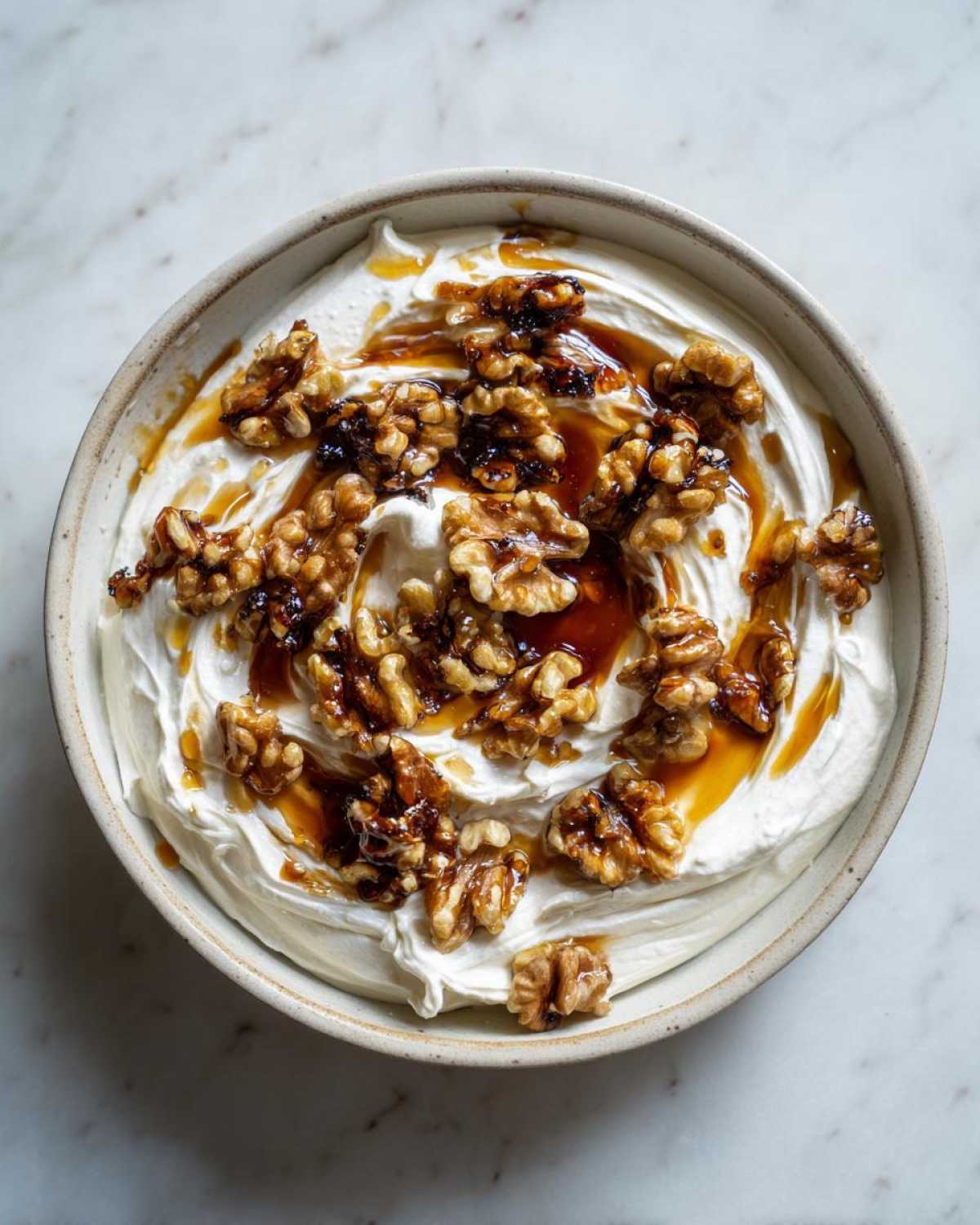 Overhead view of creamy whipped ricotta dip topped with candied walnuts and a drizzle of honey or syrup.