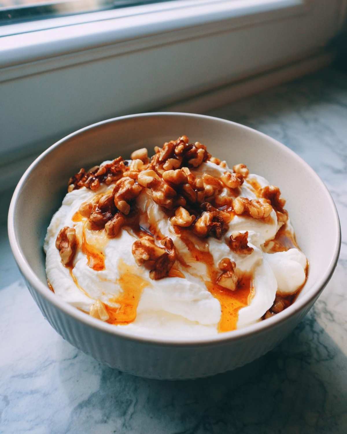 Close-up of a bowl of fluffy whipped ricotta dip topped with caramelized walnuts and a drizzle of honey.