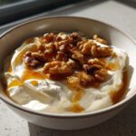 A close-up of a bowl containing creamy whipped ricotta dip, drizzled with honey and topped with toasted walnuts.
