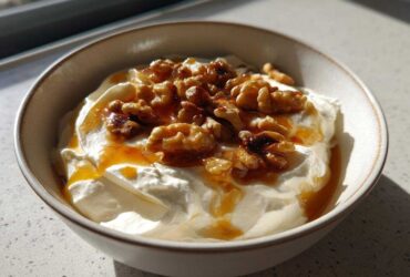 A close-up of a bowl containing creamy whipped ricotta dip, drizzled with honey and topped with toasted walnuts.