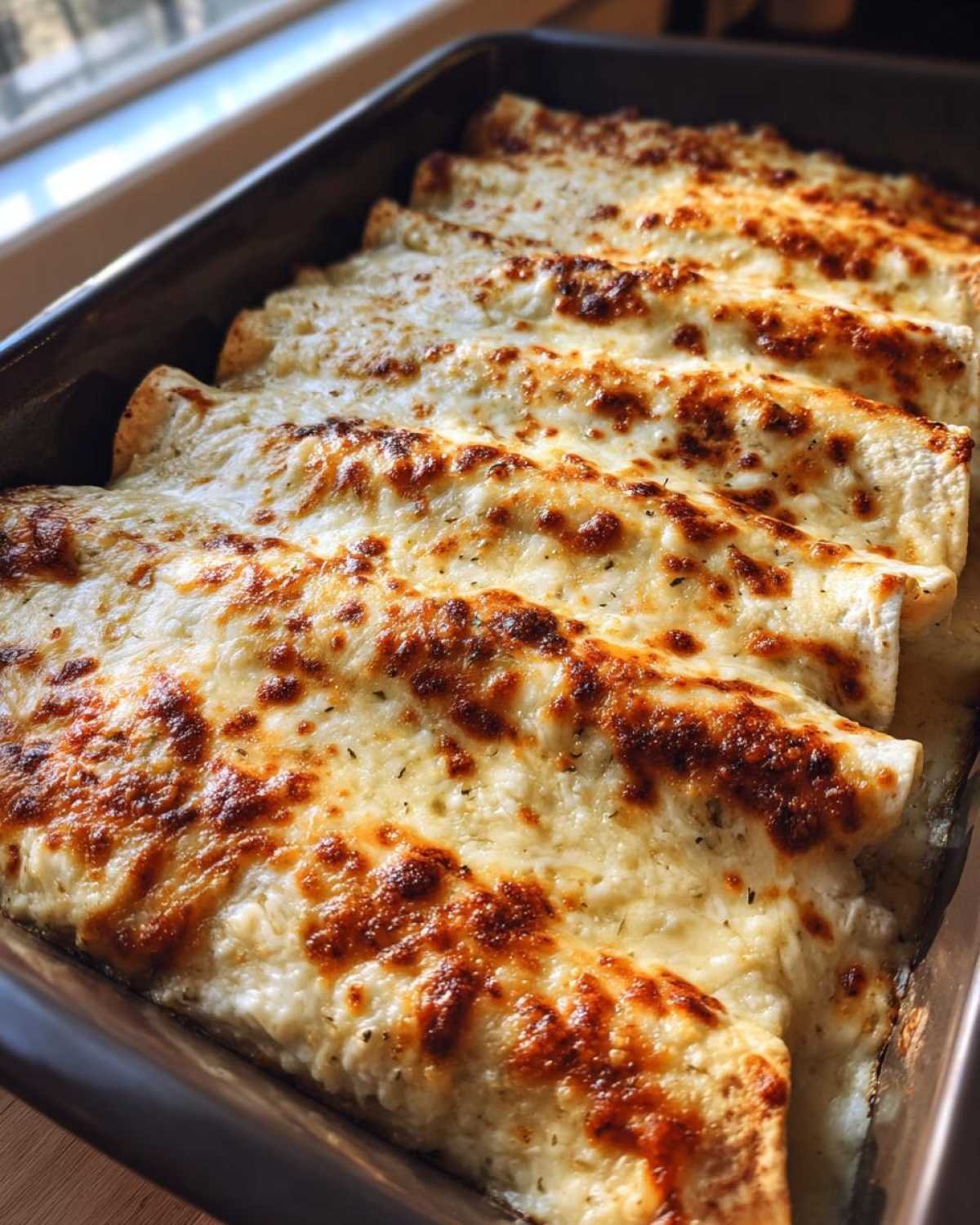 Close-up of baked white chicken enchiladas covered in bubbly, browned cheese sauce in a baking dish.