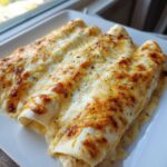 Three rolled white chicken enchiladas smothered in melted, bubbly white sauce and golden-brown cheese.