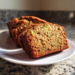 Close-up of two thick slices of moist zucchini banana bread showing green shreds of zucchini baked inside.