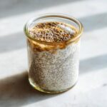 Close-up of creamy Chia Pudding made with chia seeds soaking in milk, topped with more seeds and a swirl of sweetener.