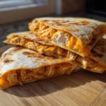 Close-up of stacked, golden-brown Chicken Quesadillas slices overflowing with shredded chicken and melted orange cheese.