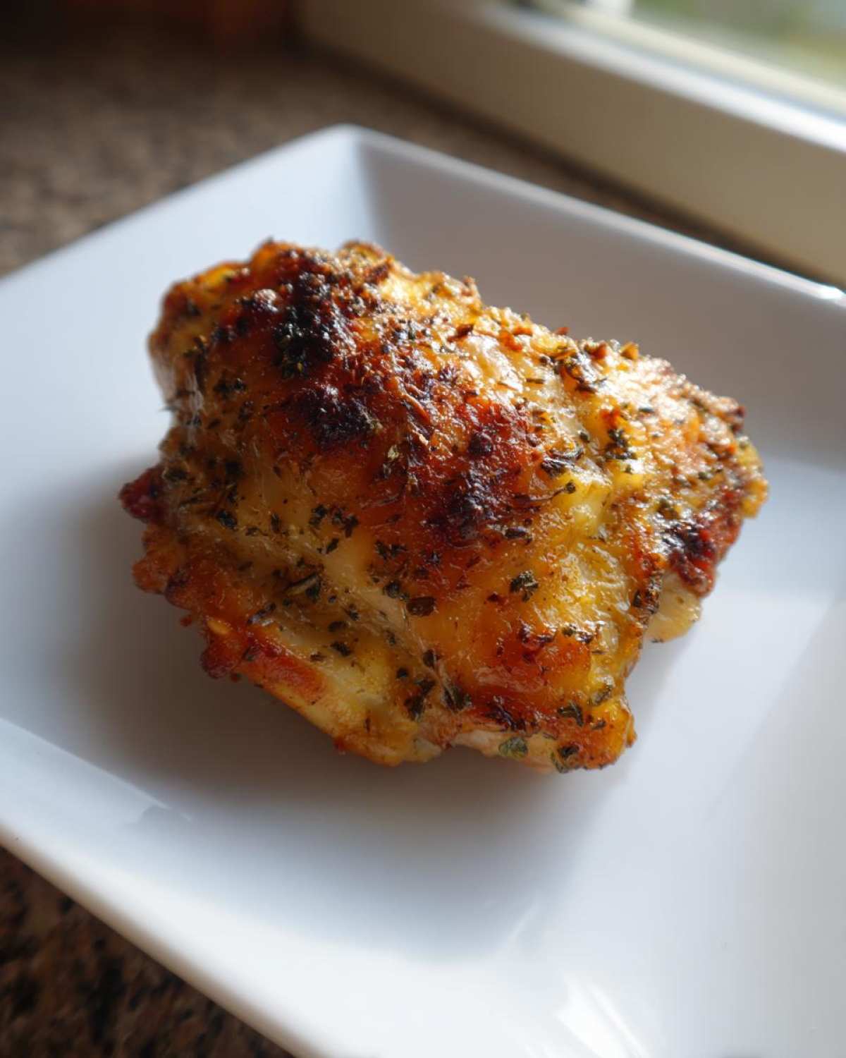Close-up of a perfectly cooked Air Fryer Garlic Parmesan Chicken Thighs with a golden, seasoned, and slightly charred top.