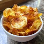 Close-up of a white bowl filled with golden brown, seasoned Air Fryer Potato Chips.