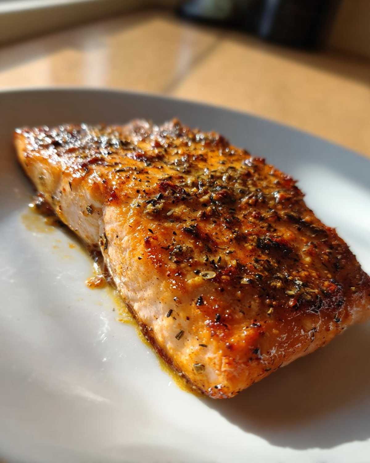 Close-up of a perfectly cooked Air Fryer Salmon fillet, seasoned heavily with herbs and spices, resting on a white plate.