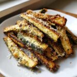 A close-up of crispy, seasoned Air Fryer Zucchini sticks topped with grated Parmesan cheese on a white plate.