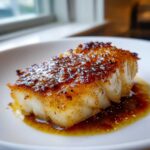 Close-up of a flaky white fish fillet, perfectly cooked Baked Honey Cod, with a dark, caramelized honey glaze.