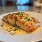 A perfectly cooked fillet of Baked Marry Me Salmon topped with melted cheese and fresh parsley, resting in a pool of creamy sauce.