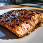 A close-up shot of a perfectly cooked fillet of Baked Salmon with Sweet and Savory Glaze, glistening under bright light.