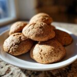 A close-up shot of several soft, cracked Banana Bread Cookies stacked on a white plate, bathed in sunlight.