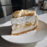 A perfect slice of Banana Pudding Cheesecake with Vanilla Wafer Crust, topped with whipped cream and fresh banana slices.
