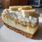 A cross-section slice of Banana Pudding Cheesecake with Vanilla Wafer Crust, topped with whipped cream and fresh banana slices.