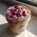 Close-up of berry topped Overnight Oats prepared in a glass mason jar, sitting in sunlight.