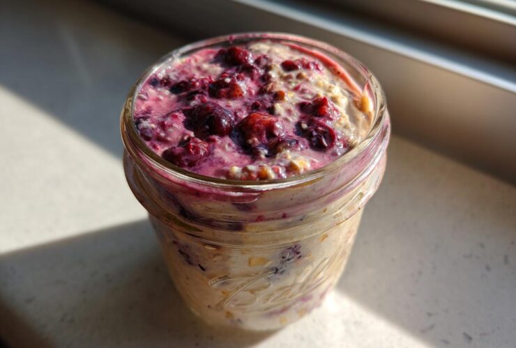 Close-up of berry topped Overnight Oats prepared in a glass mason jar, sitting in sunlight.