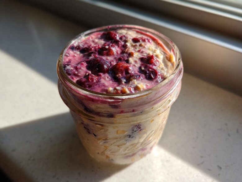 Close-up of berry topped Overnight Oats prepared in a glass mason jar, sitting in sunlight.