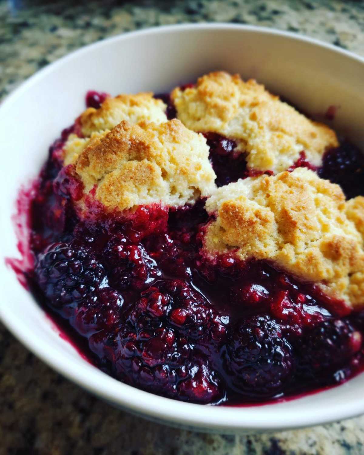 Close-up of a warm serving of Blackberry Cobbler with golden biscuit topping over juicy, dark berries.