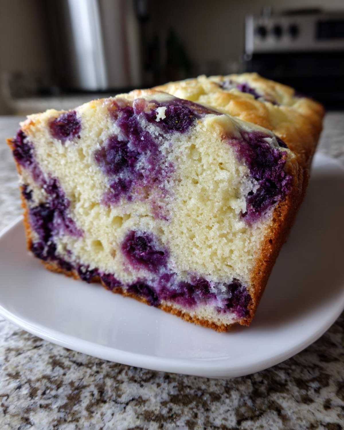Close-up of a slice of moist Blueberry Cream Cheese Bread Loaf showing vibrant purple blueberries in the light yellow cake.