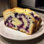 Two thick slices of moist Blueberry Cream Cheese Bread Loaf showing vibrant purple blueberry swirls in the yellow cake.