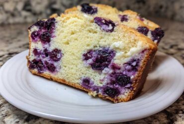 Two slices of moist Blueberry Cream Cheese Bread Loaf showing swirls of purple blueberries and white cream cheese filling.