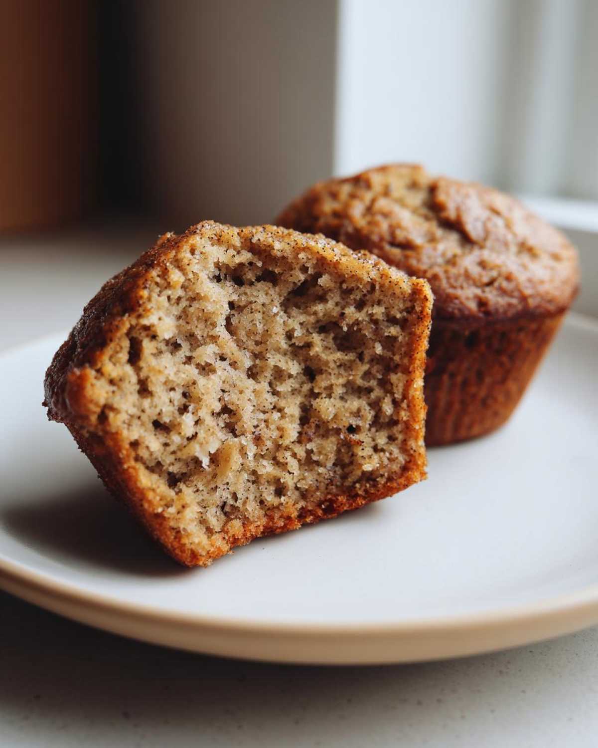Close-up of a Brown Sugar Banana Muffin cut in half showing its moist, speckled crumb texture.