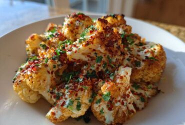 Close-up of roasted Cauliflower Elote florets topped with a creamy white sauce, fresh cilantro, and red chili flakes.