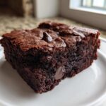 A thick, dark square of Chewy Fudgy Brownies with a shiny, cracked top and visible chocolate chips.