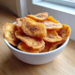 A white bowl filled with crispy Cinnamon Sugar Air Fryer Banana Chips, coated in sparkling sugar.