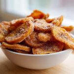 A white bowl filled with crispy Cinnamon Sugar Air Fryer Banana Chips, coated heavily in sparkling sugar.