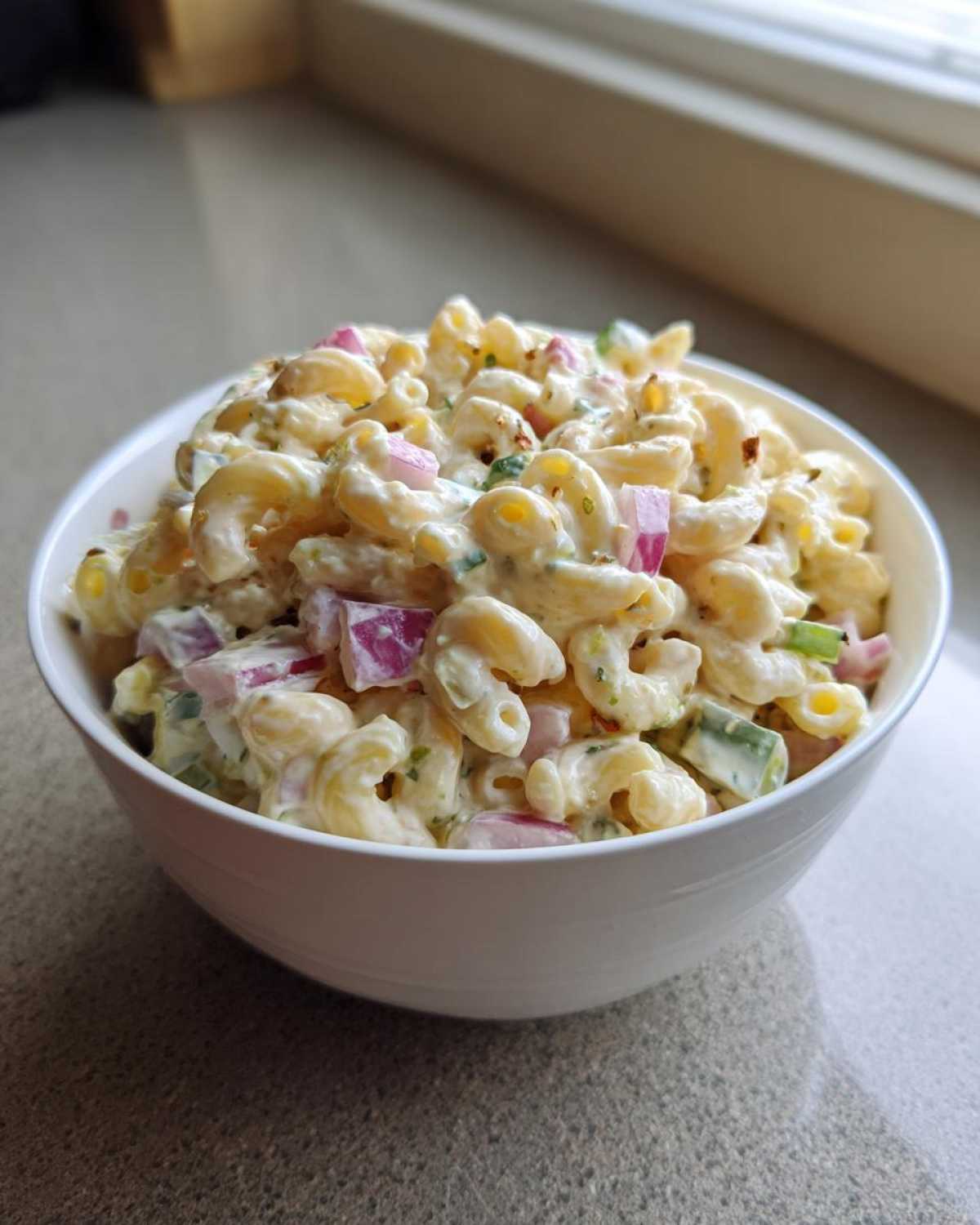 A white bowl filled with creamy Classic Homemade Macaroni Salad featuring elbow pasta, red onion, and celery.